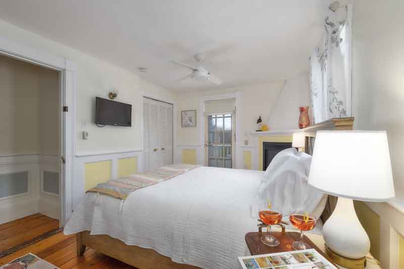 A cozy bedroom featuring a large bed, a ceiling fan, and a TV on the wall, complemented by warm lighting and decorative elements.