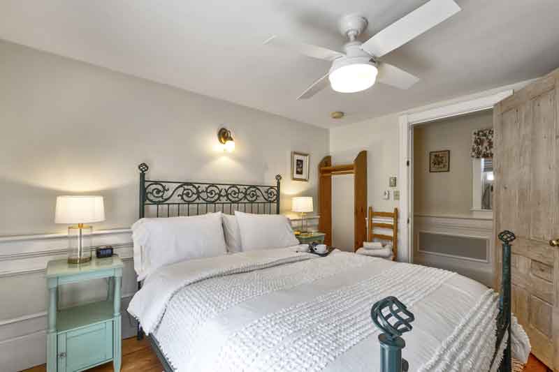 A cozy bedroom featuring a wrought-iron bed, side lamps, and a ceiling fan.