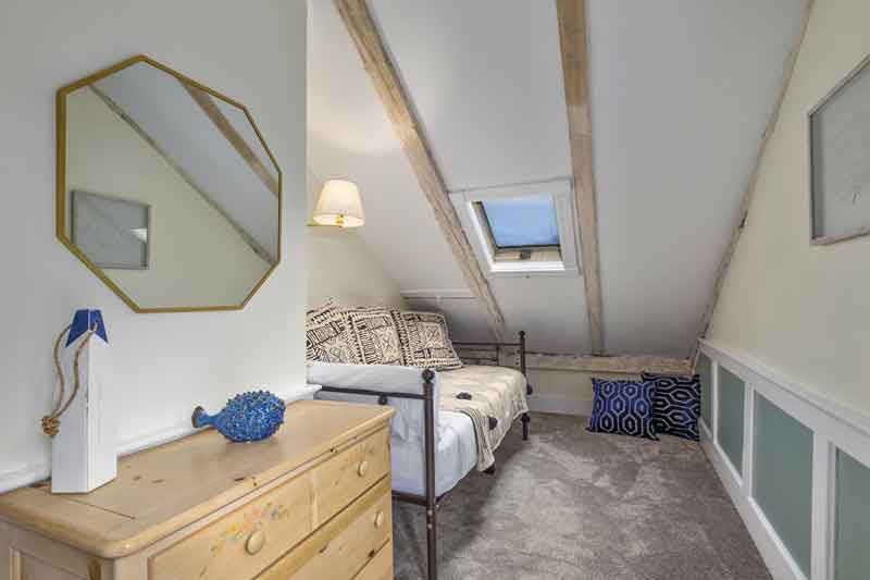 A cozy attic bedroom featuring sloped ceilings, a double bed with patterned linens, and a wooden dresser.