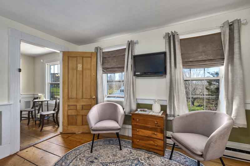 Cozy interior with two armchairs, a wooden dresser, and a television by large windows.