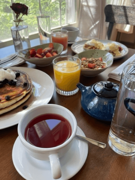 A table set for breakfast featuring pancakes, fruit, juice, tea, and a blue teapot.