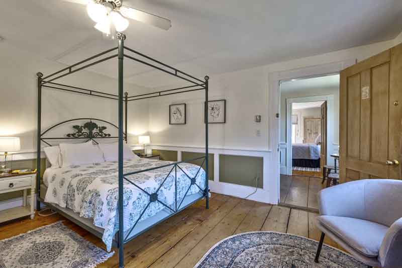 A cozy bedroom featuring a four-poster bed, patterned rug, and natural light.