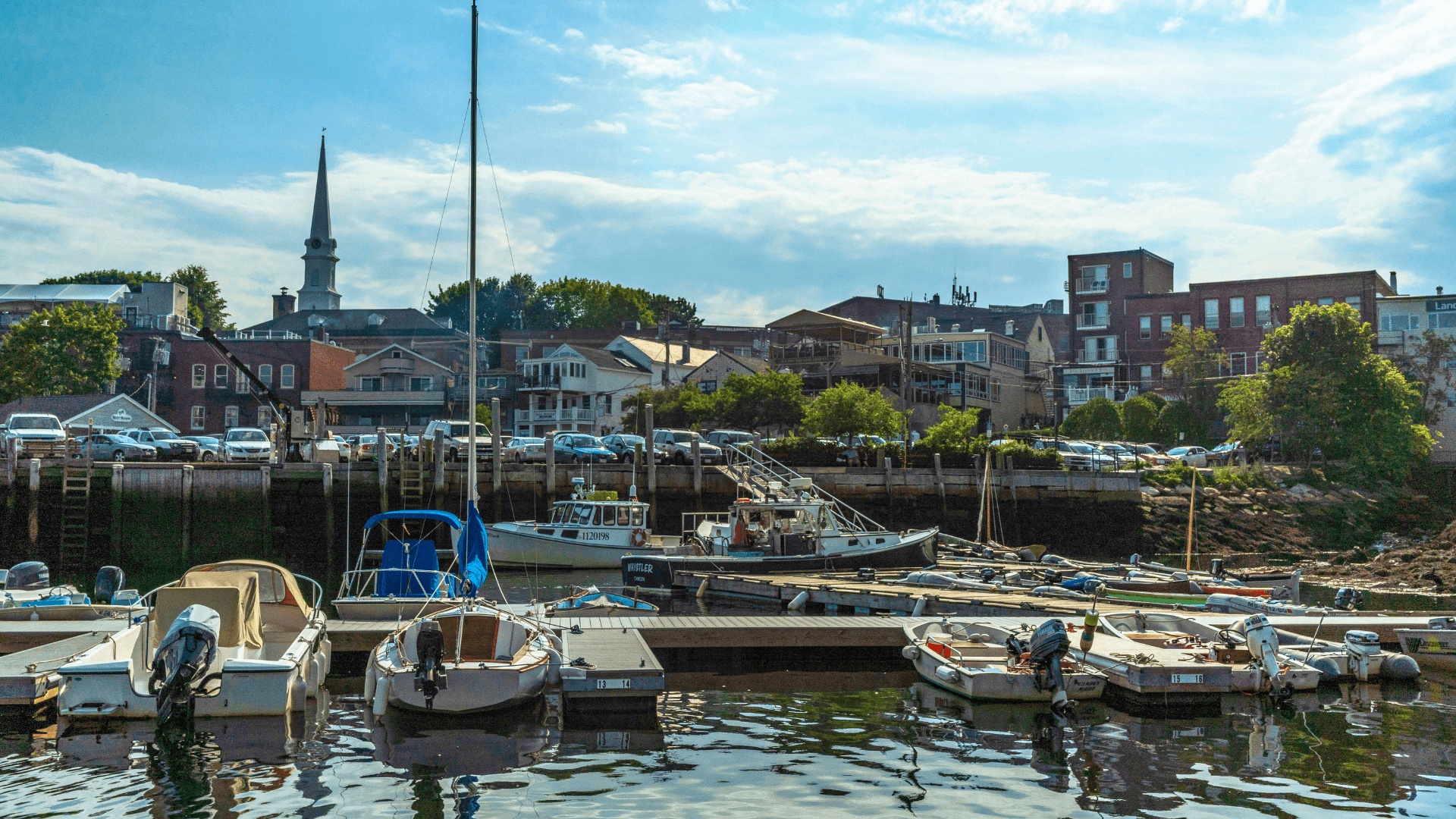 A scenic view of a marina with boats docked and a quaint town skyline in the background.