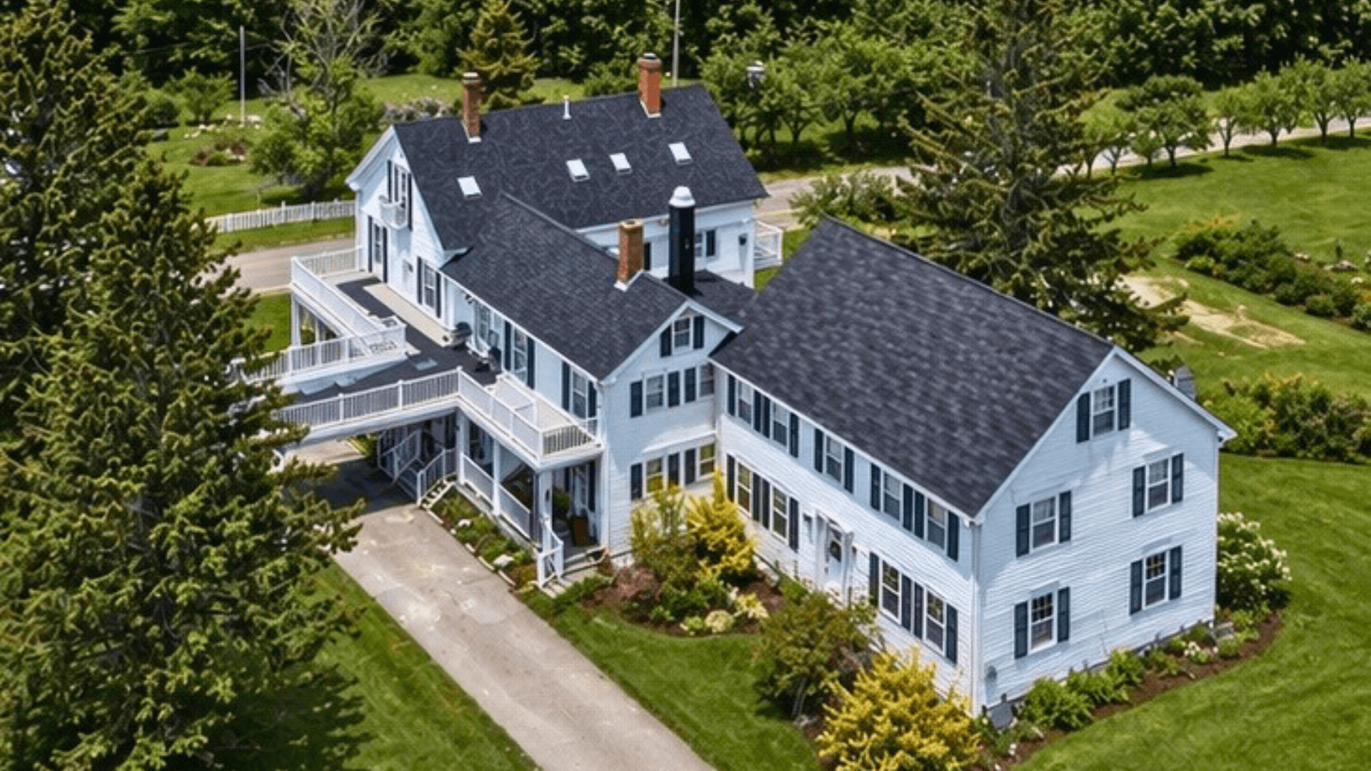 Aerial view of a large white farmhouse with a black roof surrounded by greenery.