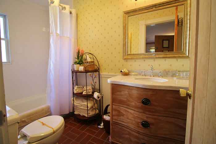 A cozy bathroom featuring a wooden dresser, a mirror, a shower curtain, and a small shelving unit with towels.