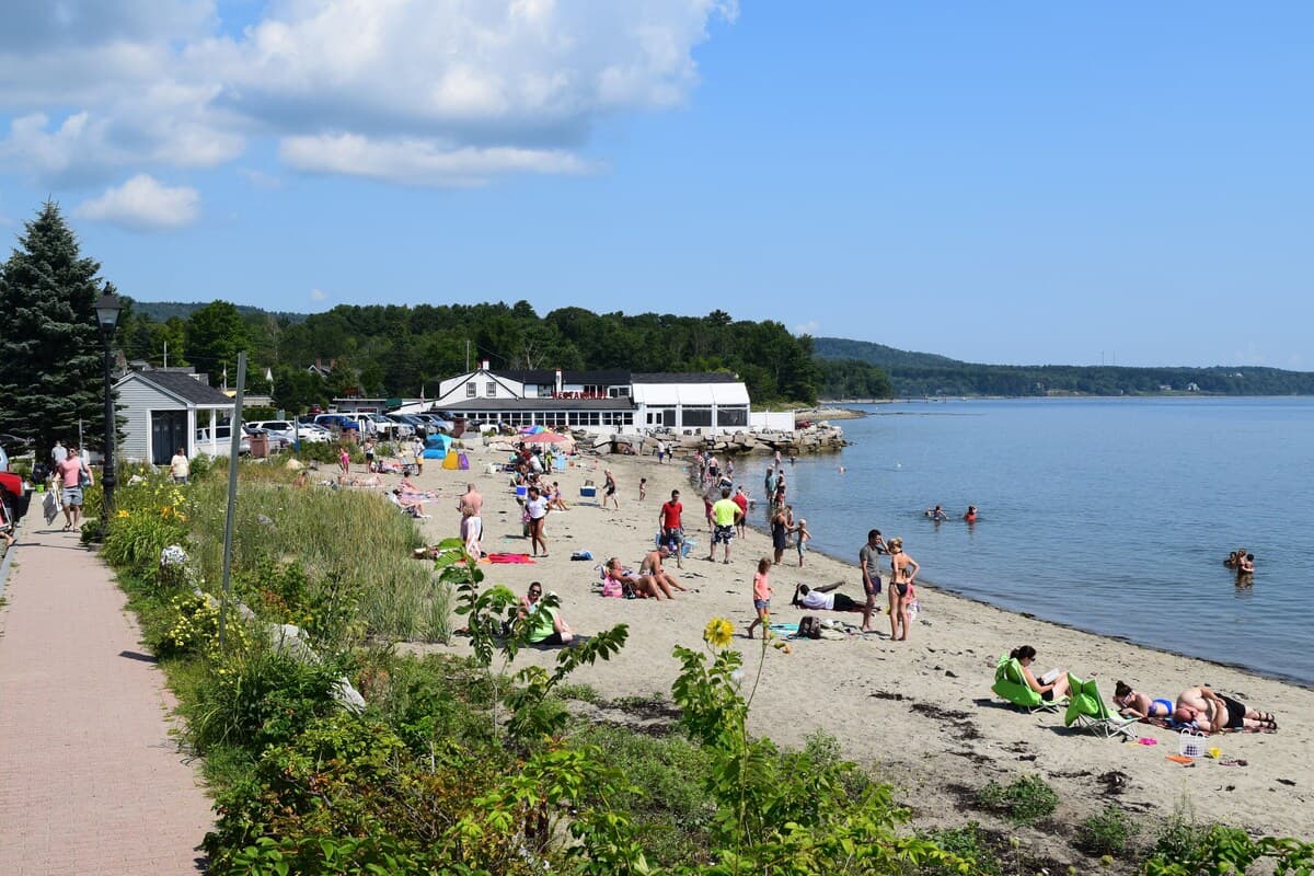 A busy beach scene with people sunbathing and swimming near a waterfront restaurant.