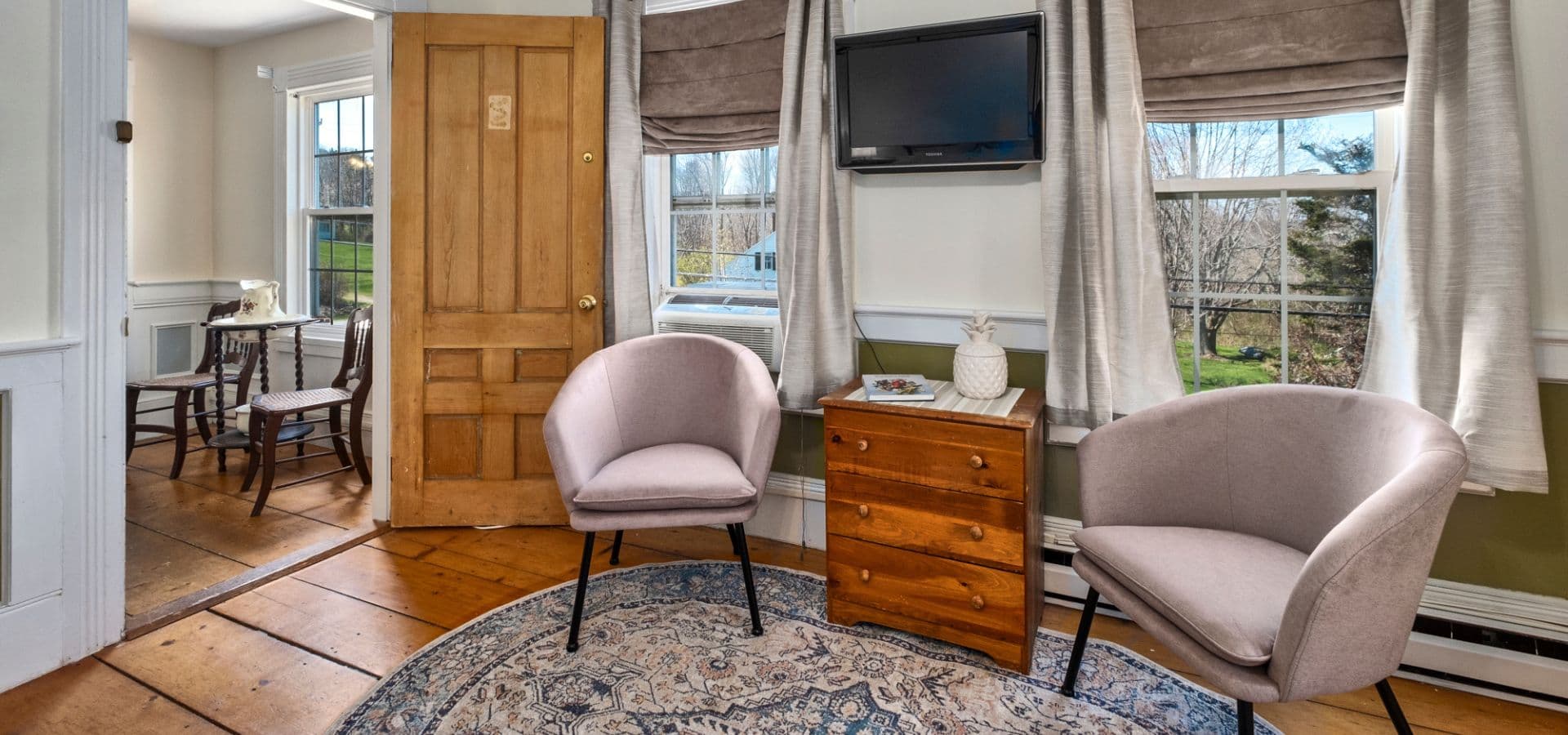 Cozy sitting area featuring two chairs, a small wooden table, and a TV against a well-lit window.