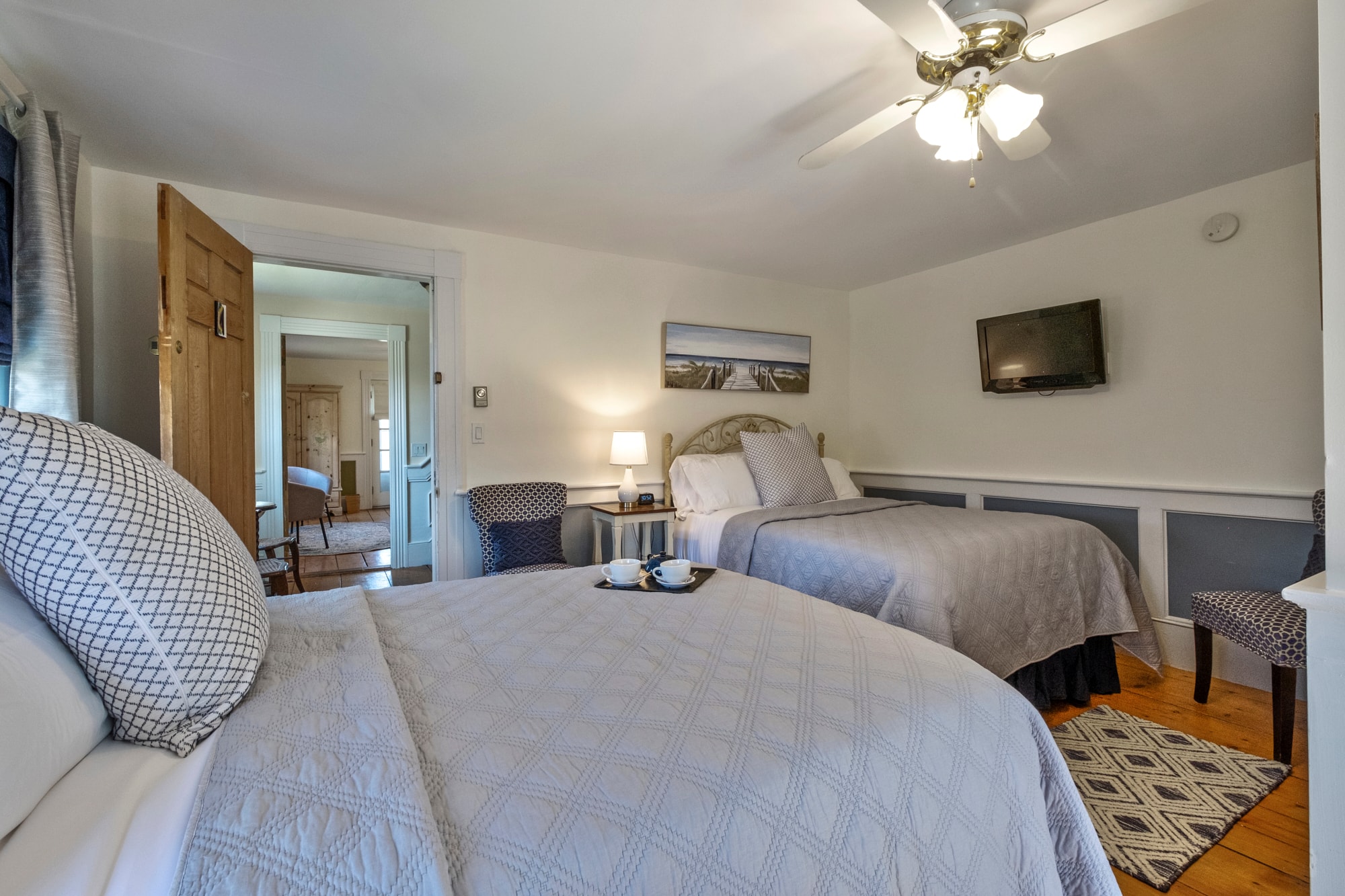 A cozy bedroom featuring two beds, a ceiling fan, a TV, and a warm, welcoming ambiance.